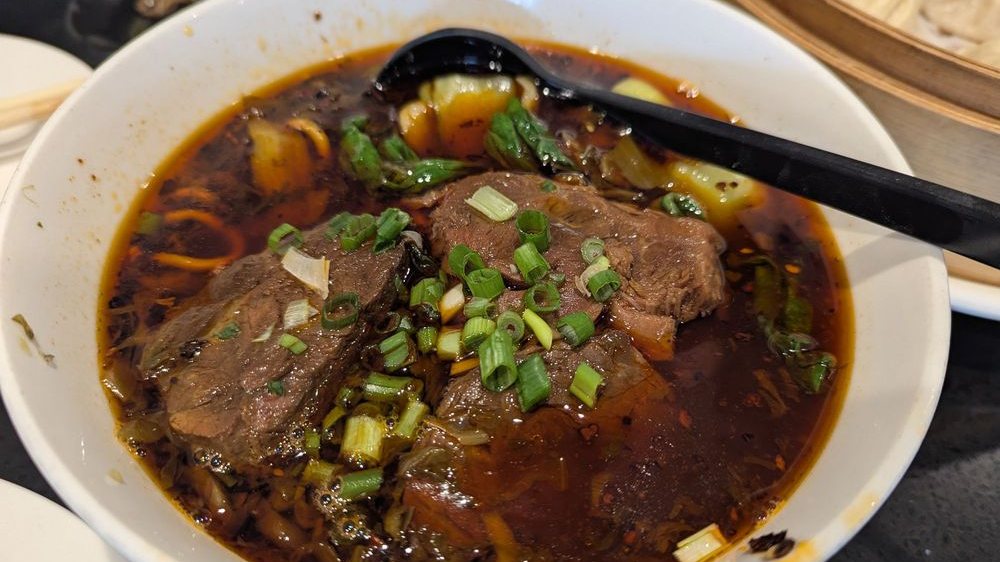 A bowl of spicy braised beef noodle soup topped with scallions