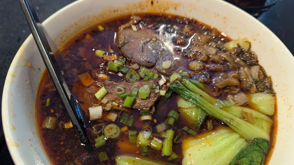 Spicy beef noodle soup with pickled vegetables, bok choy and scallions